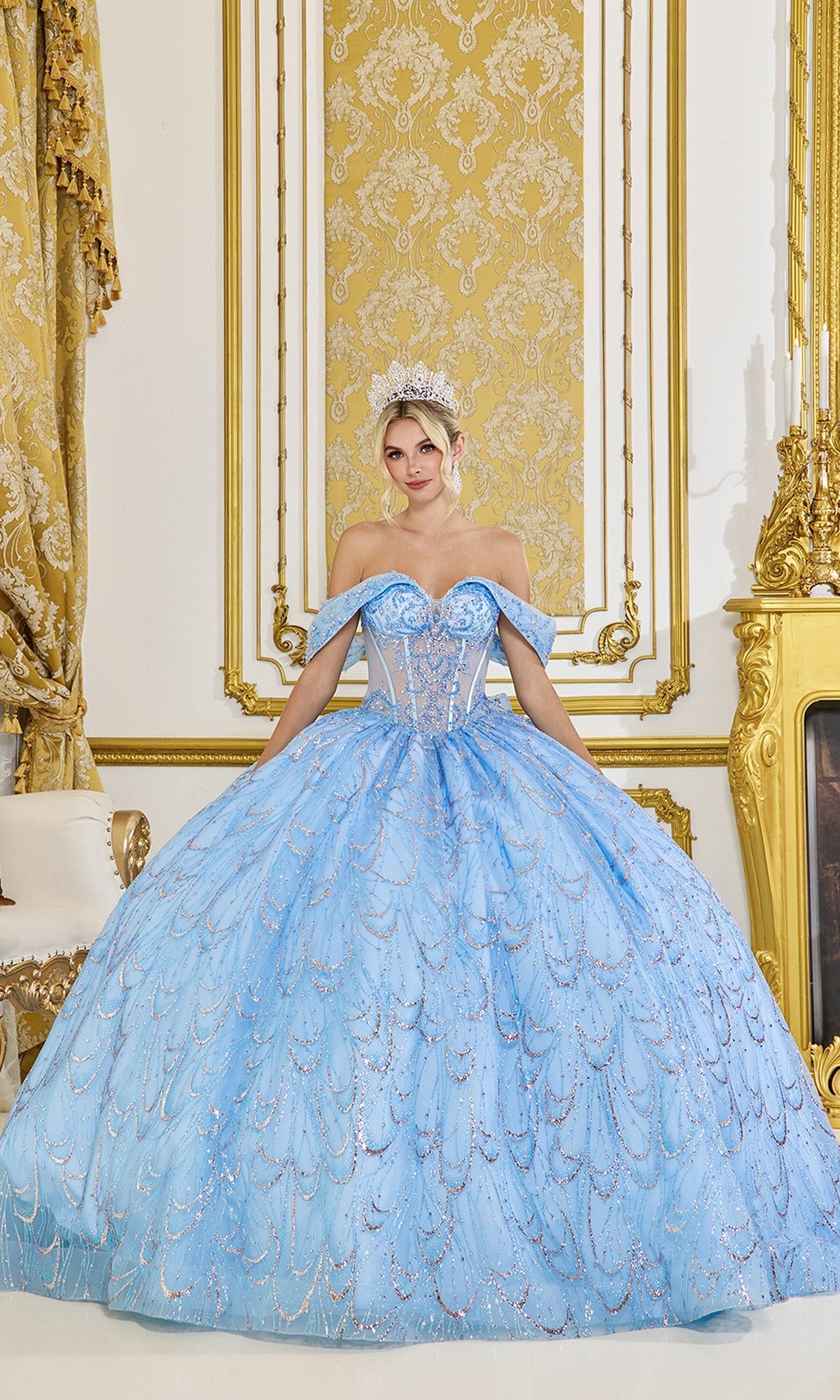 A woman in the Quinceanera Dress 5076 by Dancing Queen in Bahama Blue and a tiara stands in an ornate gold and white room with decorative curtains and a fireplace.